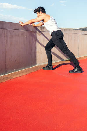 rear view of a sportsman stretching legs on a concrete wall, concept of urban sport and healthy lifestyle, copy space for text, vertical photoの写真素材