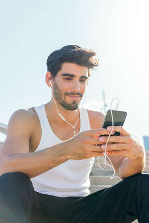 vertical photo of a handsome sportsman with earphones listening to music and consulting his phone,...