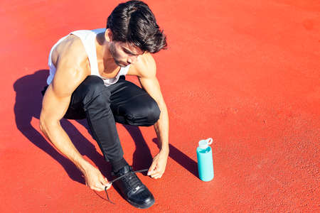 handsome runner tying his running shoes next to a water bottle, urban sport concept and healthy lifestyle, copy space for textの写真素材