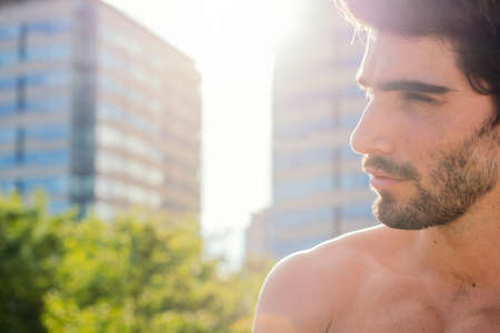 profile portrait of a handsome shirtless sporty man at sunset in front of city buildings, concept of...
