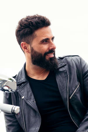 portrait of a handsome bearded man dressed in leather leaning on his motorcycle, concept of freedom...