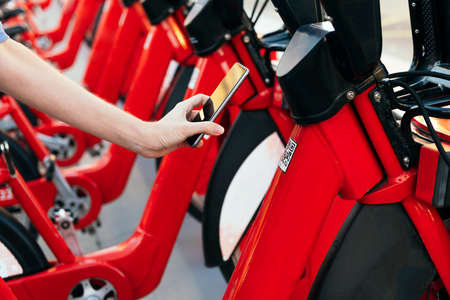 hand of an unrecognizable person using the phone to scan Qr code and unlock a bike from the rental station, concept of ecology and sustainable mobility against climate change, copy space for textの写真素材
