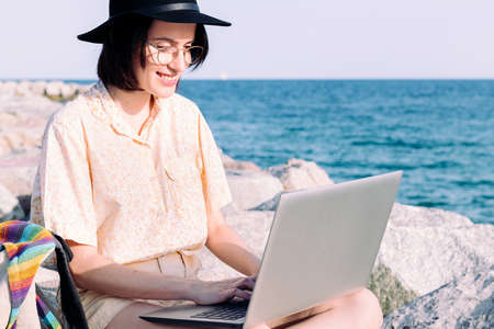 portrait of a young traveler girl working with laptop and backpack by the sea, concept of digital nomad and blogger lifestyleの写真素材