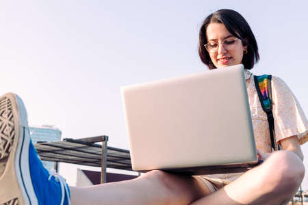 young woman working in the city with her computer and backpack, concept of technology, youth and...