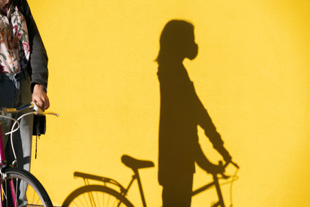 shadow of a woman on a bicycle wearing a protective mask on a colorful yellow wall, concept of protection against covid and sustainable mobility, copy space for textの写真素材