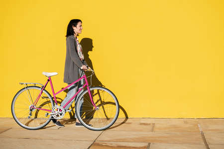 happy young girl walking in front of a colorful yellow wall with her pink retro bike, concept of...