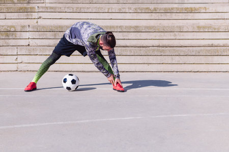 unrecognizable sportsman stretching next to his football ball in a concrete soccer court, concept of healthy lifestyle and urban sport in the city, copy space for textの写真素材