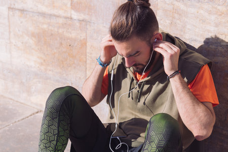 attractive sportsman putting on earphones to listen to music from his smart phone, concept of technology and urban sport lifestyle in the city, copy space for textの写真素材
