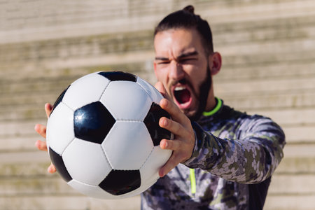 football ball in the hands of a sportsman screaming in a concrete soccer court, selective focus on the ball, concept of healthy lifestyle and urban sport in the cityの写真素材
