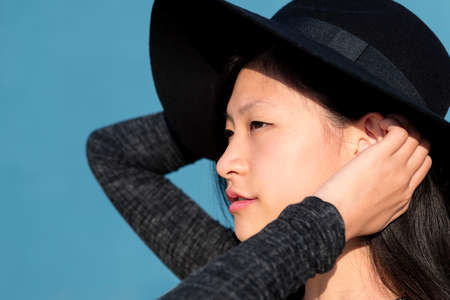 profile portrait of an elegant and beautiful asian woman in a hat on blue background, concept of fashion and lifestyle, copyspace for textの写真素材