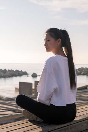 young asian woman sitting relaxed after meditate by the sea at sunrise, relaxation and mental health...
