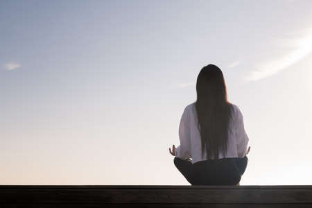rear view of a young woman with long hair meditating at sunrise, concept of relaxation and mental...