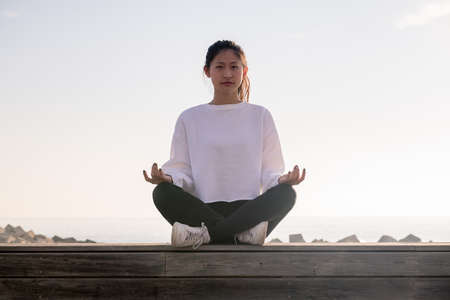 young asian woman sitting meditating at sunrise, concept of relaxation and mental health, copy space for textの写真素材