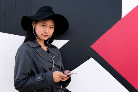 young beautiful classy chinese woman with earphones listening music from her phone, concept of technology and modern lifestyle, copyspace for textの写真素材