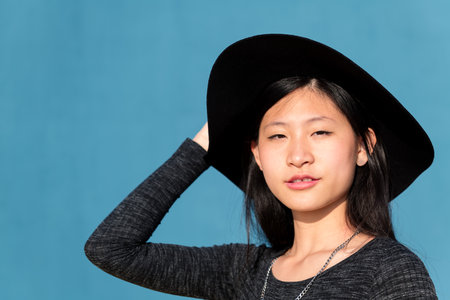 portrait of an elegant and beautiful asian woman in a hat on blue background, concept of fashion and lifestyle, copyspace for textの写真素材