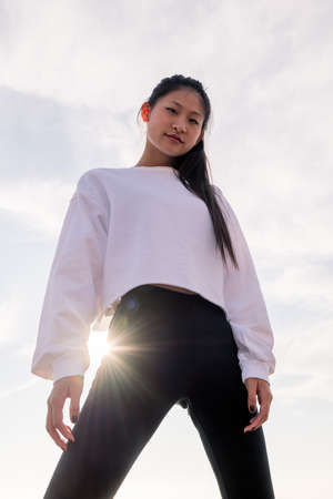 vertical photo of a powerful asian sportswoman posing confident smiling defiant at camera, concept of sport and healthy lifestyle, copyspace for textの写真素材