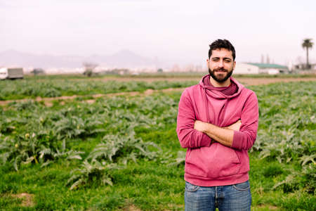 young entrepreneur farmer in front of his farm field planted with artichoke plants, concept of...