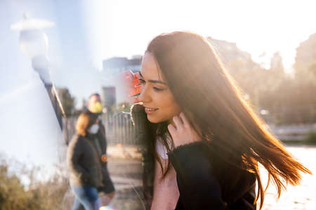 young woman looking at the reflection of two unrecognizable people wearing protective masks on the street, concept of hope and back to normality, double exposure and flare effectの写真素材