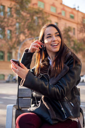 vertical portrait of a happy woman putting on the earphones of her phone, concept of communication...