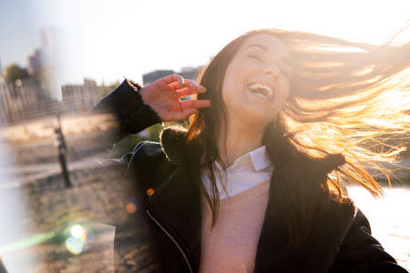 joyful young woman laughing on the street at sunset, concept of happiness and urban lifestyle,...