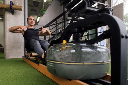 sportsman training his strength in the gym with a water rowing machine, active and sporty lifestyle...