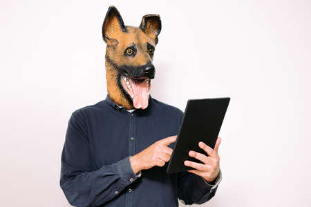 person with a dog mask typing in a digital tablet on white background, concept of technology and...