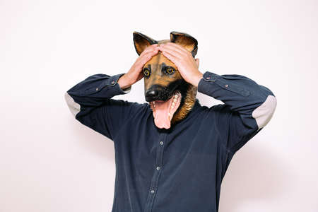 person in dog mask holds hands to head in surprise or concern on white background