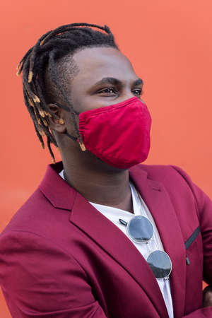 vertical portrait of a stylish african man with protective mask to match his suit on a red background, concept of elegance and fashionable lifestyleの写真素材