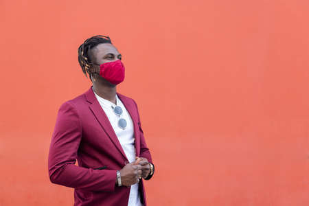 elegant african man with protective mask to match his suit on a red background, copy space for text, concept of elegance and fashionable lifestyleの写真素材