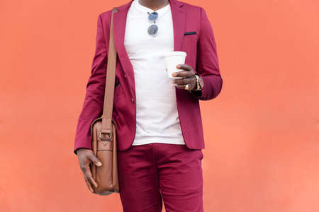 unrecognizable elegant black businessman dressed in suit with briefcase holds coffee in his hand in front of red background, copy space for textの写真素材