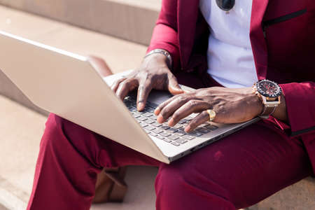 detail of the hands of an unrecognizable black man working with his laptop computer sitting on a staircase in the city, concept of technology and remote workの写真素材
