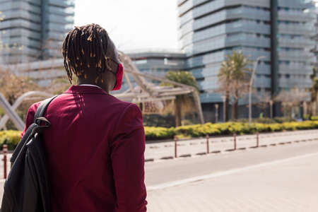 rear view of a black businessman walking around the city with a red mask to match his suit, concept of elegance and fashionable lifestyle, copy space for textの写真素材