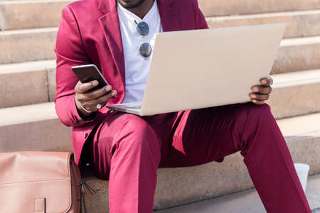unrecognizable elegant black businessman working outdoors with laptop and smart phone, technology...