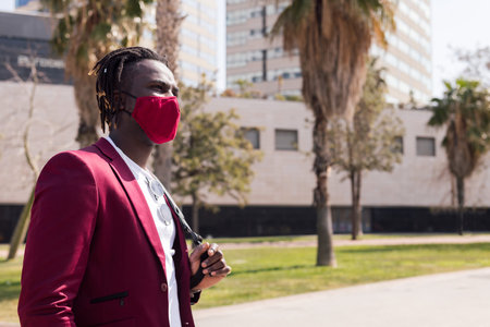 african businessman walking around the city with a red mask to match his suit, concept of elegance...