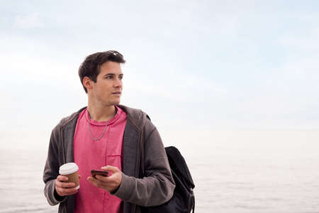 young man with a coffee using a mobile phone outdoors, concept of technology and communication, copy...