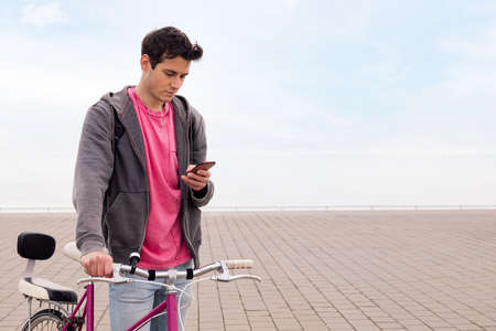 young man holding a bike while looking his mobile phone, concept of technology and sustainable urban transportation, copy space for textの写真素材