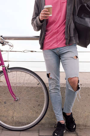 vertical photo of an unrecognizable young man with a coffee next to a vintage bike, concept of...