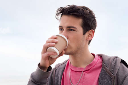 portrait of a handsome young student drinking a cup of coffee outdoors, concept of urban lifestyle, copy space for textの写真素材