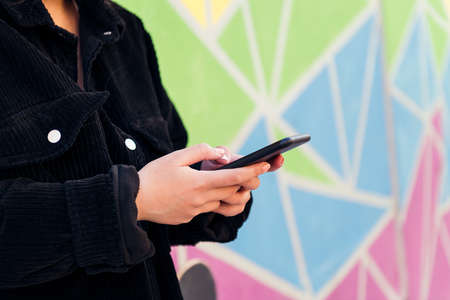 close up of the hands of an unrecognizable young woman typing on her cell phone against a colorful wallの写真素材