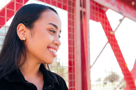portrait of a smiling young asian woman outdoors leaning against a red fenceの写真素材