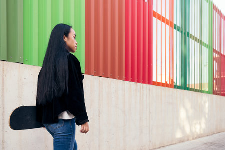 rear view of a young asian woman walking down the street with her skateboard in her handの写真素材