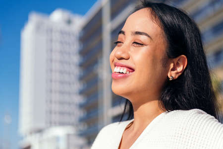 happy young asian woman smiling outdoors at city with the sun shining on her faceの写真素材
