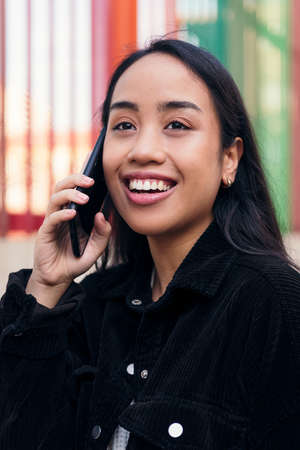 vertical portrait of a smiling young asian woman talking on the phone outdoorsの写真素材