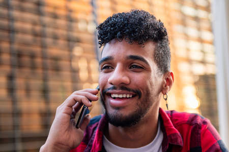 portrait of young latin man talking on the phone happy and smiling, concept of technology and urban lifestyleの写真素材