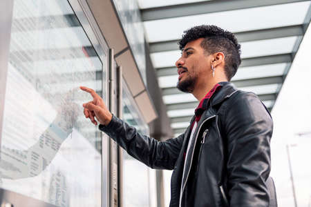 young latin man consulting the public transportation map at the bus stop, concept of sustainable transportation and urban lifestyleの写真素材