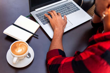 hand of an unrecognizable man typing on a laptop computer at a coffee shop table, concept of...