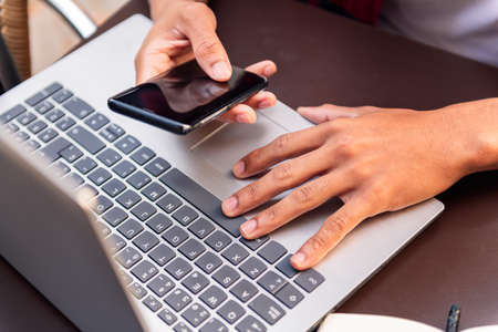 hands of an unrecognizable man working with his computer and phone, concept of technology and urban lifestyleの写真素材