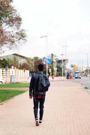 rear view of an unrecognizable stylish young man walking through the city with a backpack, concept of urban lifestyleの写真素材