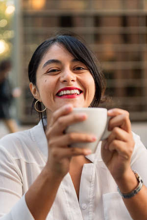 vertical photo of a woman smiling looking at camera with a cup of coffee in her hands, concept of urban lifestyleの写真素材