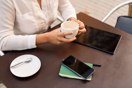 unrecognizable businesswoman drinking a cup of coffee and working with phone and tablet, concept of digital entrepreneur and urban lifestyleの写真素材